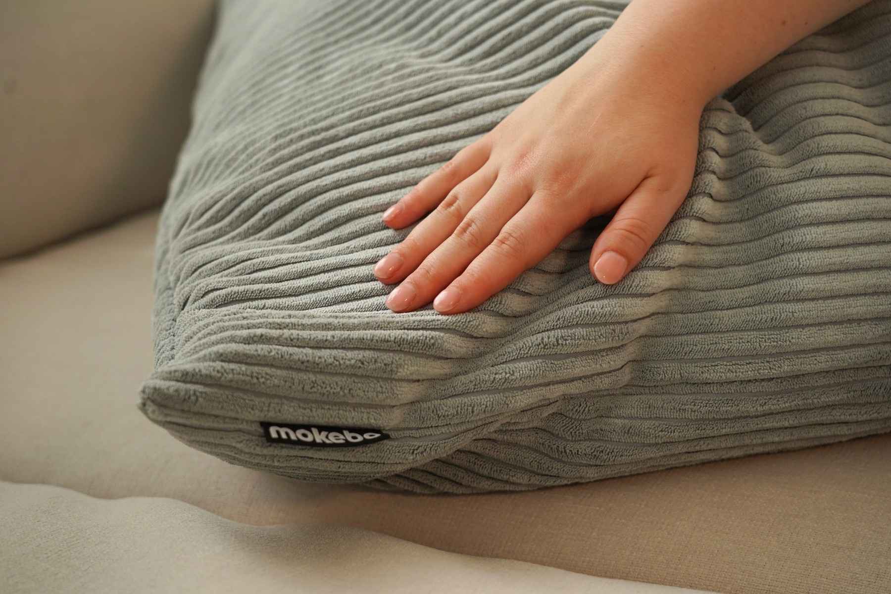Cordkissen in hellgrau. Hand streicht über das Kissen. 
