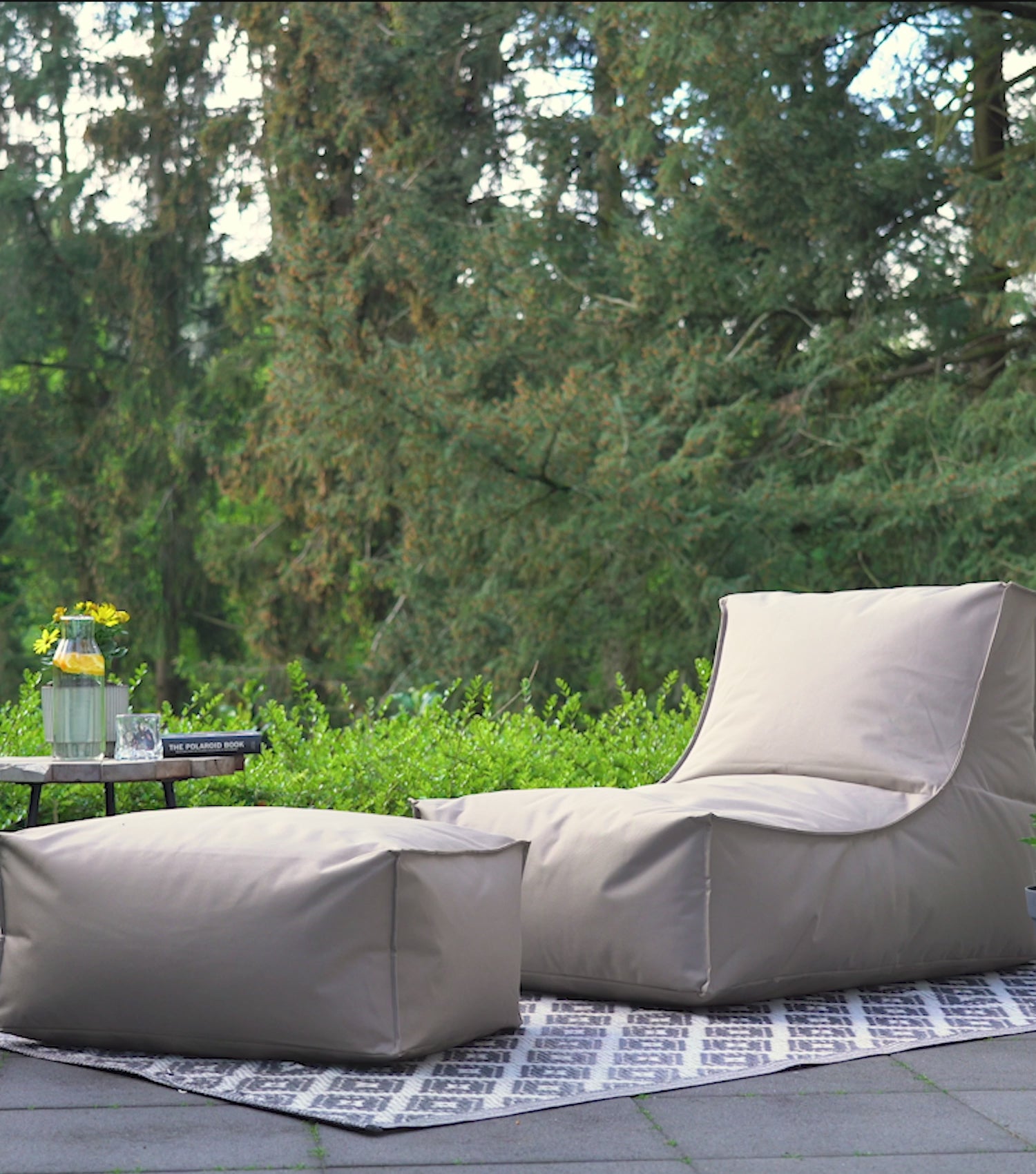 Produktvideo Outdoor Sitzsack Sitzsessel 'Der Sundowner' in khaki. Mann setzt sich auf den Sitzsack und liest, legt die Füße auf den Pouf, steht auf und hüllt den Sitzsack in die Schutzhülle ein. Wasser perlt von der Schutzhülle ab. 